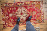 Distressed Oushak rug with a central hexagonal medallion, pinwheel elements, cherry red and ivory tones.