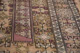 Distressed Melas rug, beige and pale blush, with geometric dragon motif and vine border.