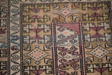 Distressed vintage Melas rug detail: geometric patterns, beige and aubergine, with foundation showing.