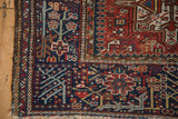 Vintage Karaja rug corner showing geometric flowers on a navy field and side tatter.
