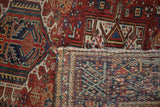 Karaja rug pile with geometric cherry red, navy patterns, hand-knotted foundation, tattered fringe.