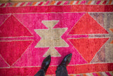 Distressed texture of a vintage Kurd runner, showing vibrant fuchsia, red, and silver geometric patterns.