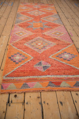 Distressed Kurd rug runner's fringed end, showing short pile and geometric coral, pink, silver patterns.