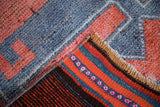 Textured, distressed blue and red pile of a Kurd rug lifted to reveal colorful striped foundation.