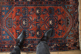 A viewer's perspective of the vintage Borchalou rug, showing its low pile and detailed geometric patterns in rust and blue.