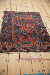Angled perspective of a vintage Borchalou rug with rust red and dark blue geometric arabesque patterns.