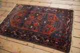 Angled view of a traditional Persian Borchalou rug with a geometric pattern in rust red and sapphire blue.