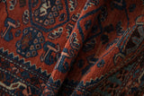 Rich texture of a folded vintage Persian rug with sapphire blue boteh motifs on a rust field.