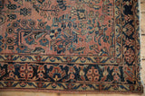 Corner view of antique Sarouk rug: dusty red field, navy floral border, tattered end.