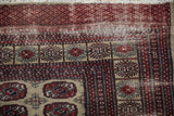 Afghani Bokhara rug corner showing cherry red, navy borders, geometric guls, and visible foundation.