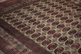 Angled close-up of vintage Bokhara rug's cherry red guls on beige field, showing varied pile.