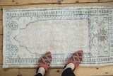 Distressed ivory Oushak prayer rug with worn pile and pale jade geometric border.