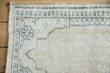 Corner of distressed Oushak rug featuring ivory, jade geometric pearl border and low worn pile.