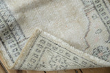 Folded vintage distressed Oushak rug corner, revealing worn pile, foundation, and ivory fringe.