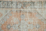 Distressed Oushak rug detail: worn dusty terracotta and ivory pile, dark brown patterns.