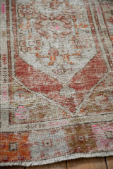 Detailed view of a distressed rug's worn pile, showing brick red and pink motifs over the exposed foundation.