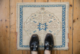 A person stands on the small vintage Oushak mat, showing its scale and blue starburst design.