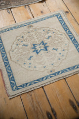 Angled view of a distressed vintage Oushak mat highlighting its sapphire blue starburst on an ivory field.