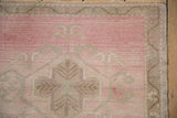 Corner of a distressed pink Oushak rug with a low pile and a meandering sand-colored vine border.
