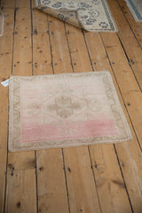 Angled view of a vintage distressed Oushak mat with soft blush, pink, and sand tones.