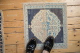 A small vintage Oushak mat with a distressed navy and blush medallion, shown top-down for scale.