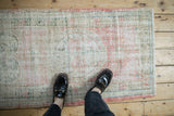 Demonstrating the scale of a distressed vintage Oushak rug with its faded blush and sage pattern.