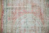 Distressed Oushak rug's hand-knotted texture with foundation wear in soft pink and sage green hues.