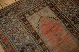 Close-up of distressed Melas rug, showing muted brick red prayer motif and floral border.