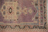 Distressed Oushak rug showing abrashed aubergine field and antique ivory meandering vine borders.