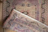Distressed Oushak rug texture and meandering vine border in aubergine, ivory, seafoam tones.