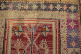 Distressed Oushak rug texture showing geometric florals in violet, faded red, and ivory.