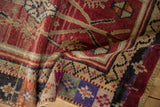 Distressed Oushak rug corner showing geometric pinwheel motifs, violet, red, and green.