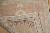 Distressed Oushak rug's folded corner reveals hand-knotted back, worn rose and beige pile.