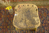 Rustic primitive stool top with weathered wood, paint splatter, holes, and plank seam.