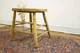 Rustic stool's chippy yellow painted legs and stretchers, with a small vase of flowers.