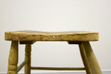 Antique stool's thick weathered wooden seat edge with paint splatter and dark patina.