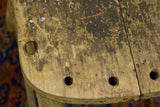 Primitive stool top with dark weathered wood, yellow chippy paint, and drilled holes.