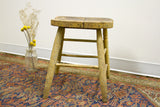 Rustic stool's weathered wood legs, showing paint splatter and dark tones.