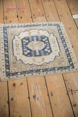 Distressed Oushak rug corner showing dusty navy vine border, intact selvage, and even wear.