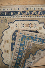Folded corner of vintage distressed Oushak rug revealing hand-knotted dusty navy, ivory vine border.