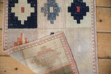 Curled corner of a vintage Oushak rug mat, revealing worn pile, navy motif, and intact selvage.