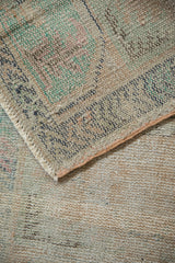 Distressed vintage Oushak rug corner, showing worn pile, visible foundation, fringe, and soft hues.