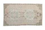 Distressed Oushak rug mat, faded cream, pale green, and brown floral medallion.