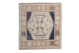 A distressed vintage Oushak square rug with a serrated navy and ivory medallion and pale coffee brown border.