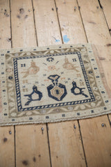 Distressed Turkish Oushak rug corner showing beige bird arabesque, navy border, and even pile wear.