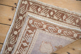 Corner detail of a distressed Oushak rug with copper finned vine border and beige textured pile.