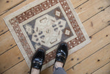 A vintage distressed Oushak square mat with a low, even pile, shown for scale reference.