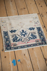 A high-angle view of a vintage Oushak square mat showing its worn texture and geometric design.