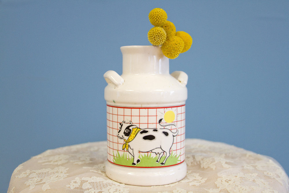 White ceramic farmhouse milk jug vase with a cow graphic on a red grid pattern.