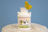 White ceramic farmhouse milk jug vase with a cow graphic on a red grid pattern.